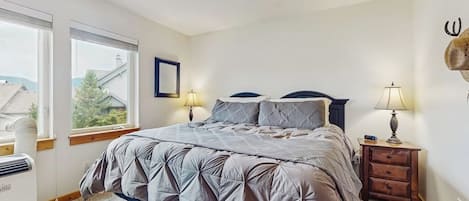 A bedroom with a bed, two bedside lamps, a heater, and a window with blinds.