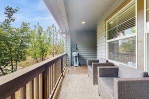 A covered porch with a grill, wicker furniture, and a view of trees. - 2 BR Townhome at the Villages at Roslyn Ridge (Ronald)
