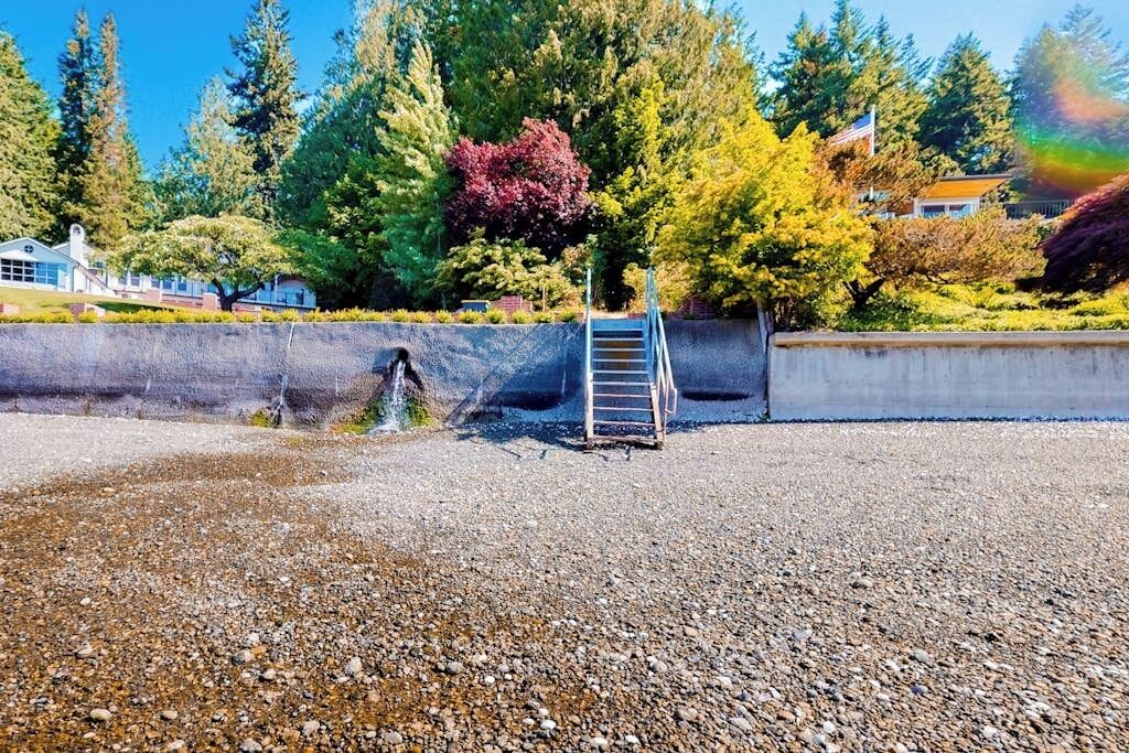A gravel area with a concrete wall, a metal ladder, and a tree with red leaves.