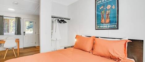A bedroom with a bed, a wardrobe, a desk, and a poster on the wall.