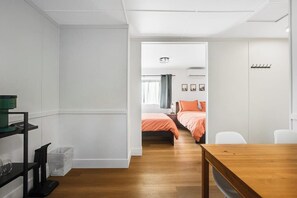 Une chambre d’hôtel moderne avec un plancher en bois, un lit avec une literie orange, un bureau avec une chaise et une petite poubelle.