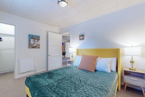 Un dormitorio con cama, mesita de noche y puerta que da a otra habitación.