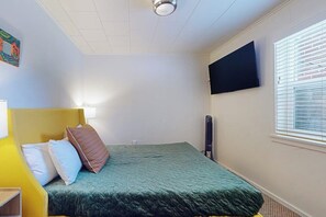 A single-bed room with a green bedspread, a mounted flat-screen TV on the wall, and a window with blinds. - 1BR Hotel Room right in Downtown Port Townsend (Port Townsend)