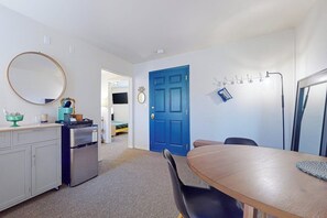 Een kleine keuken met een koelkast, een eettafel met stoelen, een blauwe deur en een kapstok.