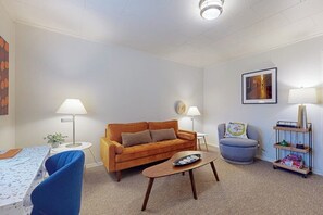 Een woonkamer met een bank, een salontafel, een lamp, een stoel en een boekenkast.