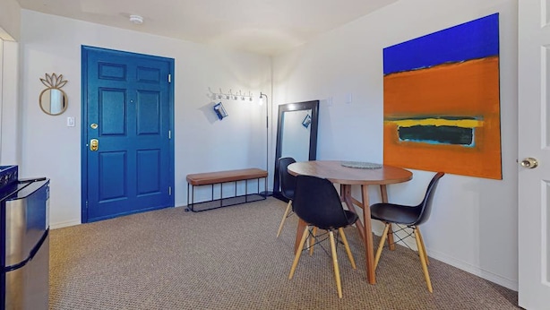 A room with a blue door, a round table with chairs, a bench, a mirror, and a large abstract painting on the wall. - 1BR Hotel Room right in Downtown Port Townsend (Port Townsend)