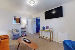A living room with a sofa, armchair, coffee table, TV, and a door leading to another room.
