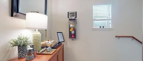 A hallway with an exit sign, a clock, a fire extinguisher, and a window.