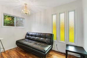 Ein Zimmer mit einer schwarzen Ledersofa, einem kleinen runden Tisch, einer Chandelüster und einem Fenster mit gelb getöntem Glas.