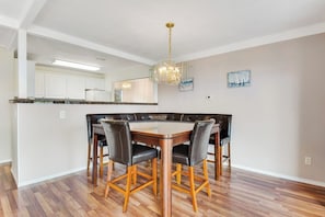 Ein Essbereich mit Holztisch und Stühlen, einer Chandelüster und einer Küche im Hintergrund.