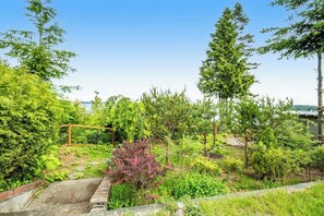 Ein Garten mit verschiedenen Bäumen und Sträuchern, einem Holzzaun und einem gepflasterten Weg.