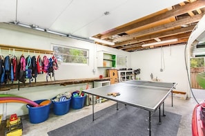 Una stanza con tavolo da ping pong, attrezzature per esercizi fisici e un appendiabiti con giacche.