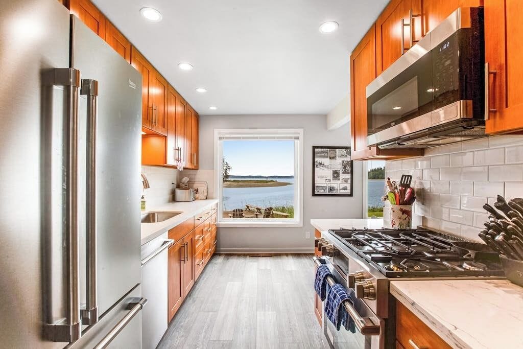 A kitchen with wooden cabinets, stainless steel appliances, a window with a view, and a tiled backsplash.