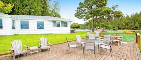 A wooden deck with outdoor furniture, a white house in the background, and a grassy yard.