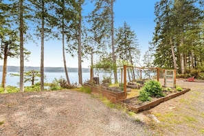 A garden with raised beds and a wooden pergola near a lake. - 1BR Bayview Dog Friendly - Fireplace (Brinnon)