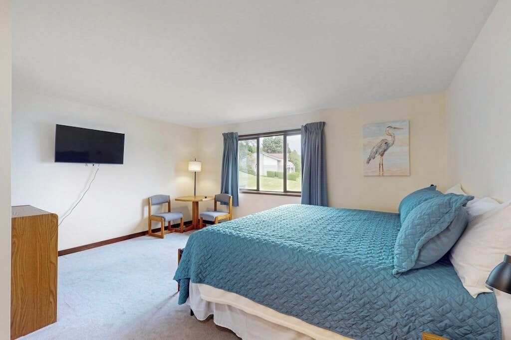A bedroom with a bed, a desk, a chair, a television, and a window with curtains.