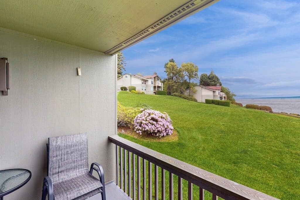 A balcony with a chair and a small table, overlooking a well-maintained lawn and houses in the distance.