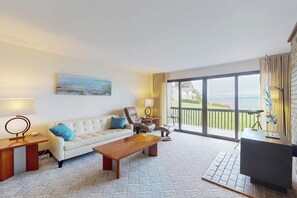 Una sala de estar con sofá, mesa de centro y sillas, un cuadro en la pared y vistas amplias por las ventanas.