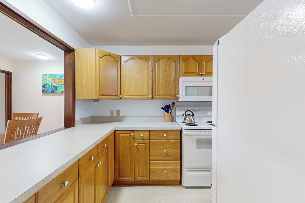Una cocina con armarios de madera, encimera blanca, microondas y hervidor.