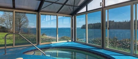 A covered swimming pool with a view of a lake and forest.