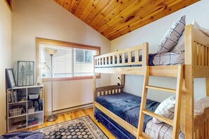 Ein Schlafraum mit Etagenbett, Fenster, Schreibtisch mit Lampe und Bücherregal.