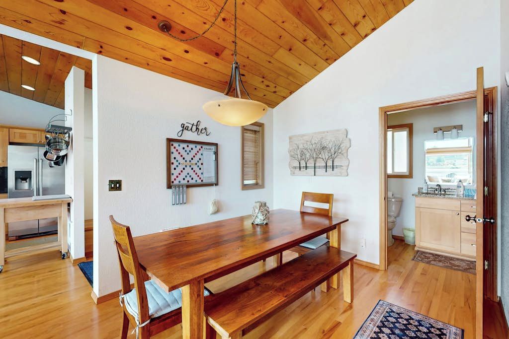 A spacious dining area with a wooden table and benches, a hanging light fixture, and artwork on the walls.