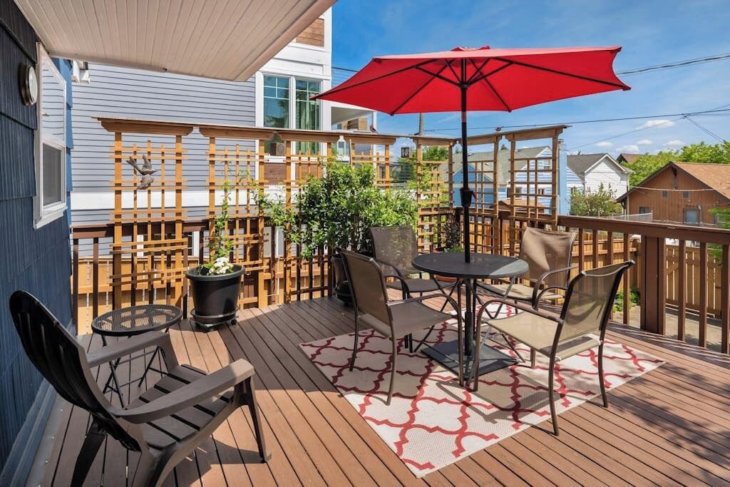Eine Terrasse im Freien mit Tisch und Stühlen, einem roten Sonnenschirm und einem Holzzaun.