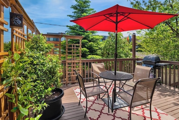 Een buitenterras met een tafel, stoelen, een rode parasol en een barbecue.