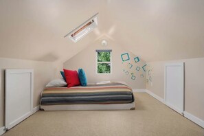 Ein Schlafzimmer mit schrägen Wänden, einem Bett mit gestreifter Bettwäsche, einem Fenster und geometrischen Wandstickern.