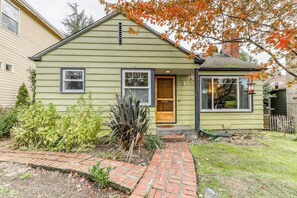 A single-story house with a brick pathway leading to the front door, surrounded by a garden with various plants. - Large 2BR Northeast Seattle - Deck - Washer Dryer (Seattle)