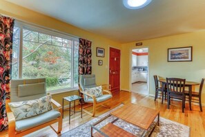 A living room with two sofas, a coffee table, and a dining table with chairs. There is a door leading to a kitchen and a window with curtains. - Large 2BR Northeast Seattle - Deck - Washer Dryer (Seattle)