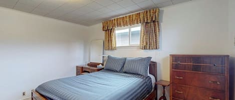 Une chambre à coucher avec un lit, une commode, une table de chevet et une fenêtre avec des rideaux.