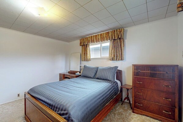 A bedroom with a bed, a dresser, a nightstand, and a window with curtains.