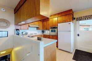 A compact kitchen with wooden cabinets, a white refrigerator, a microwave, and a sink.