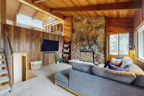 A cozy living room with a stone fireplace, a grey sofa, and a wooden staircase. - 3BR Lakefront Gas Grill - Deck - Firepit (Hoodsport)