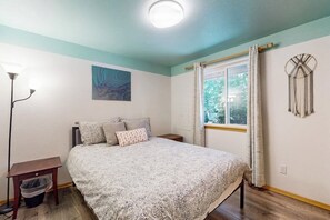 Een slaapkamer met een bed, nachtkastje, lamp, raam met gordijnen en een decoratie aan de muur.