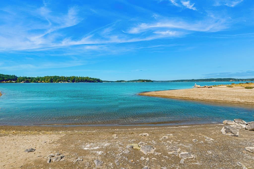 A coastal landscape with a clear sky, calm water, and a sandy beach.