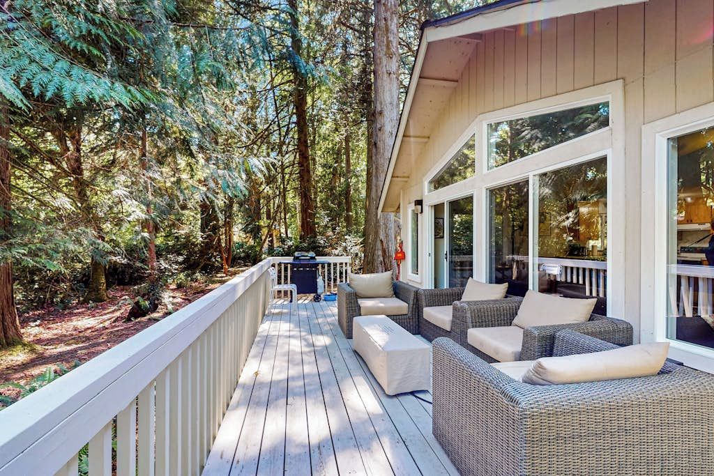 Una terraza techada con mobiliario de mimbre y vistas a un bosque.