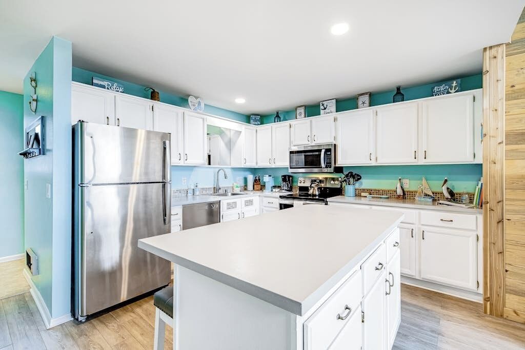A modern kitchen with white cabinets, stainless steel appliances, and a teal accent wall.