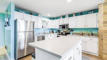 A modern kitchen with white cabinets, stainless steel appliances, and a teal accent wall.