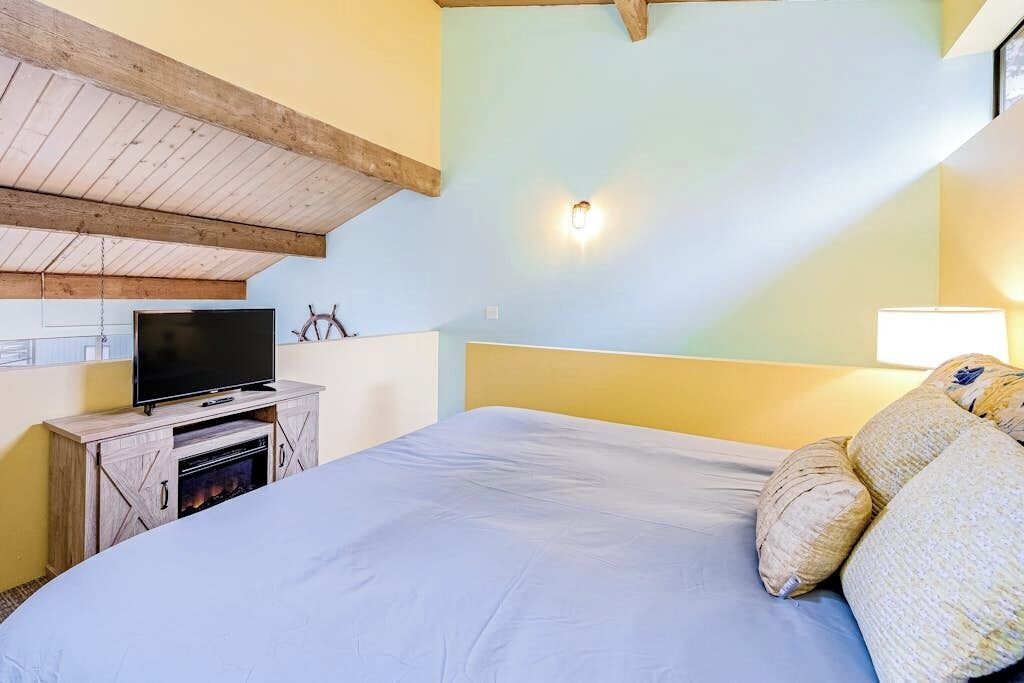 Ein Schlafzimmer mit einem Bett, einem Fernseher auf einer Holzkommode und einer Wandleuchte.