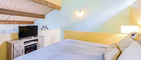 Une chambre à coucher avec un lit, un téléviseur posé sur un meuble en bois et un luminaire fixé au mur.