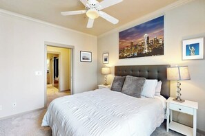 A bedroom with a large bed, a ceiling fan, a cityscape painting, and a framed picture of the Statue of Liberty. - Waterfront 1BR with fitness center & hot tub (Seattle)