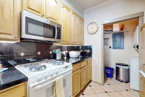 A kitchen with wooden cabinets, a microwave, a stove, and a clock on the wall. - Waterfront 1BR with fitness center & hot tub (Seattle)