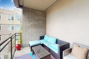 En balkon med en sofa, et lille bord og en rød vase.