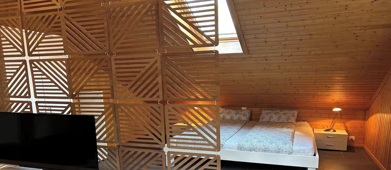 A bedroom with a bed, bedside table, lamp, and a decorative wooden partition.