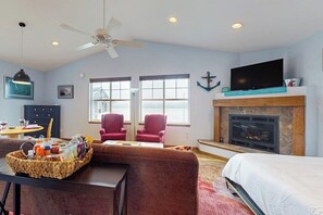 A living room with a fireplace, a television, and a ceiling fan. - 1BR Cozy Waterfront Studio Rental (Camano Island)
