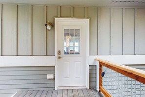 A white door with a glass panel, a metal gate, and a wooden railing on a porch with horizontal siding. - 1BR Cozy Waterfront Studio Rental (Camano Island)