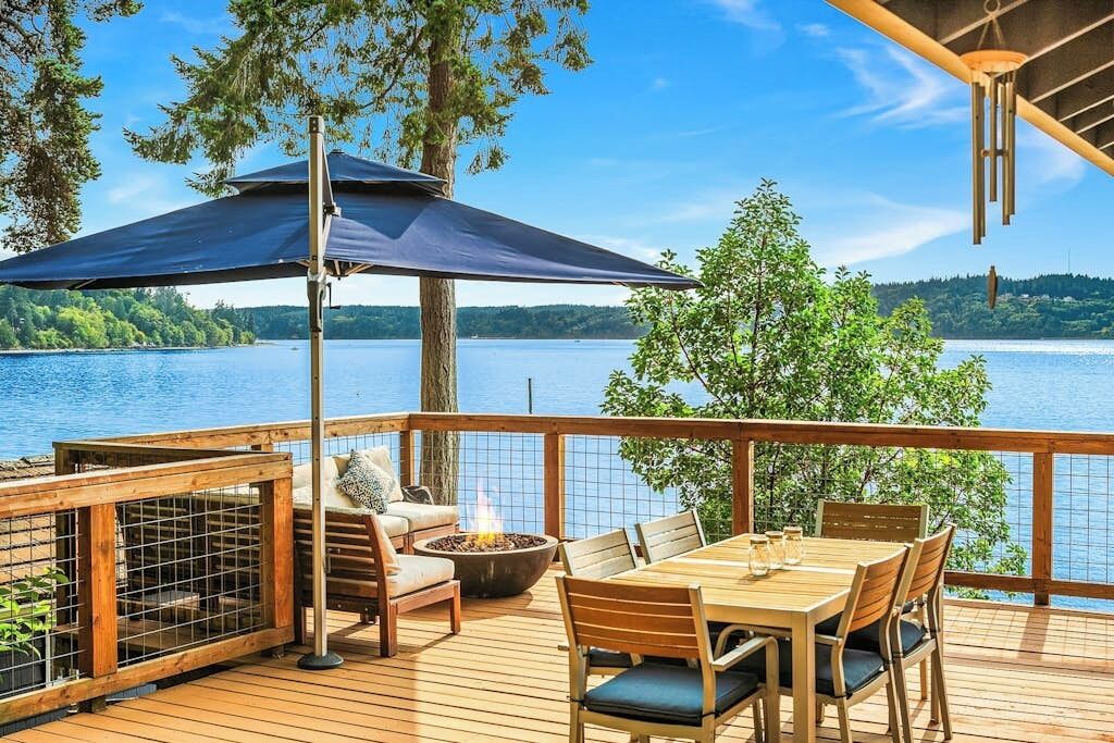 A wooden deck with a table and chairs, a fire pit, and a large umbrella.