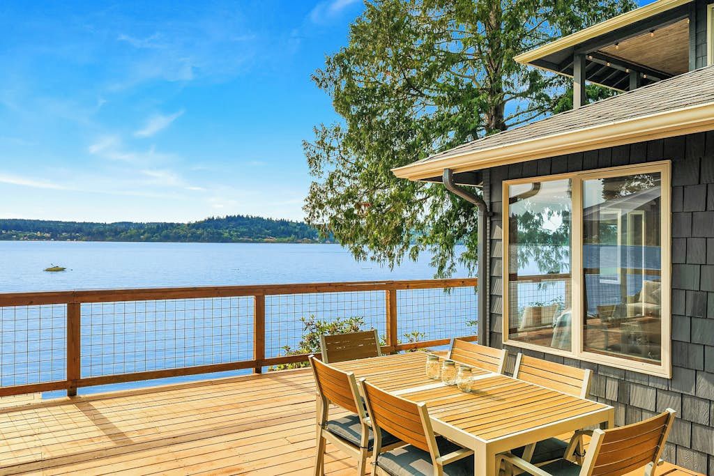 Eine Holzterrasse mit Tisch und Stühlen mit Blick auf ein Gewässer.